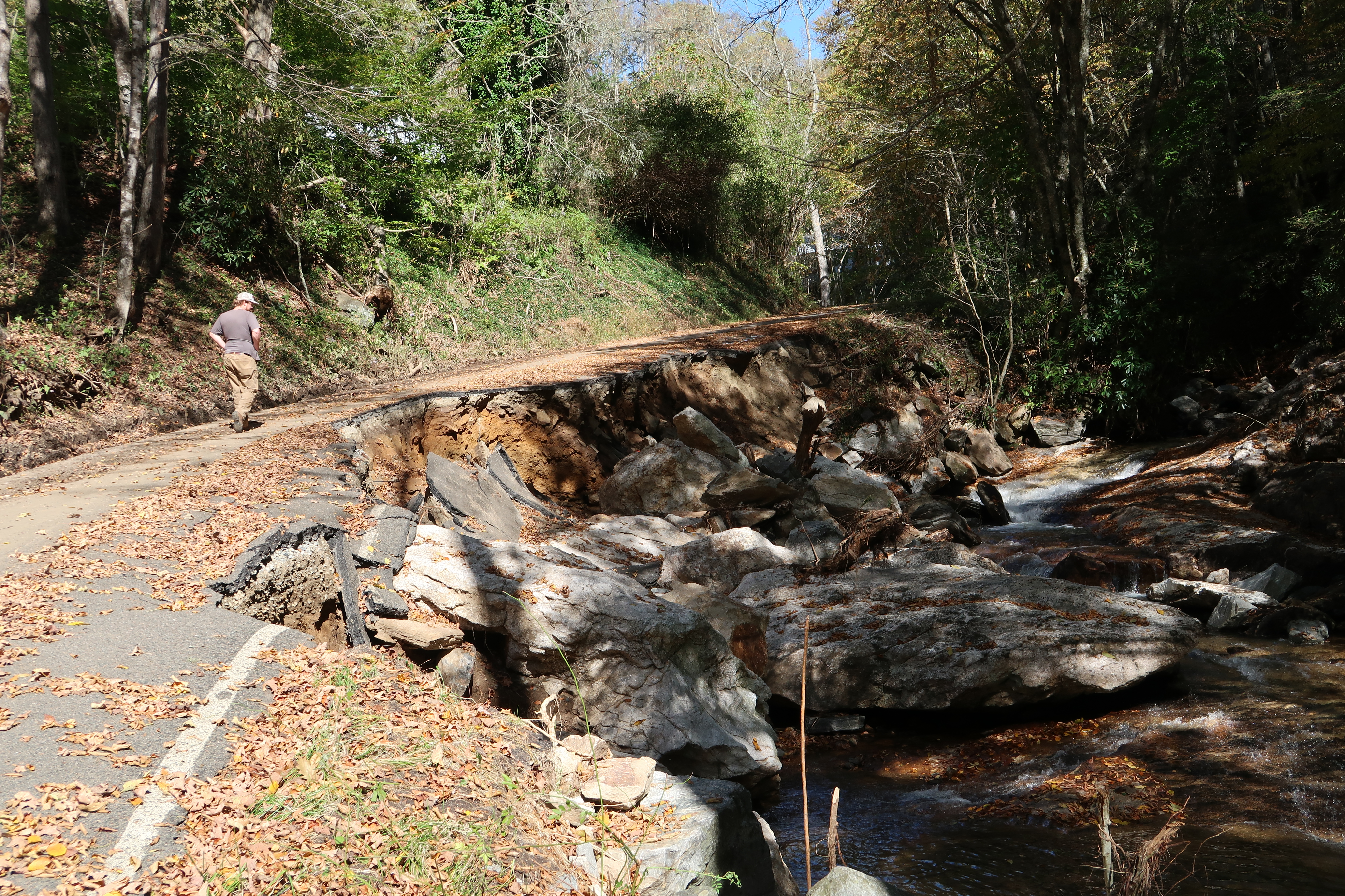 A man walks across a washed out road where a creek flooded during Hurricane Helene.